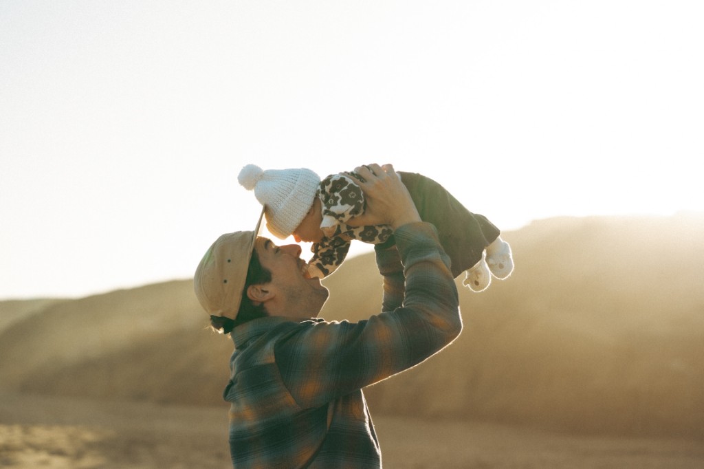Parent lifting a baby in warm golden light by the coast