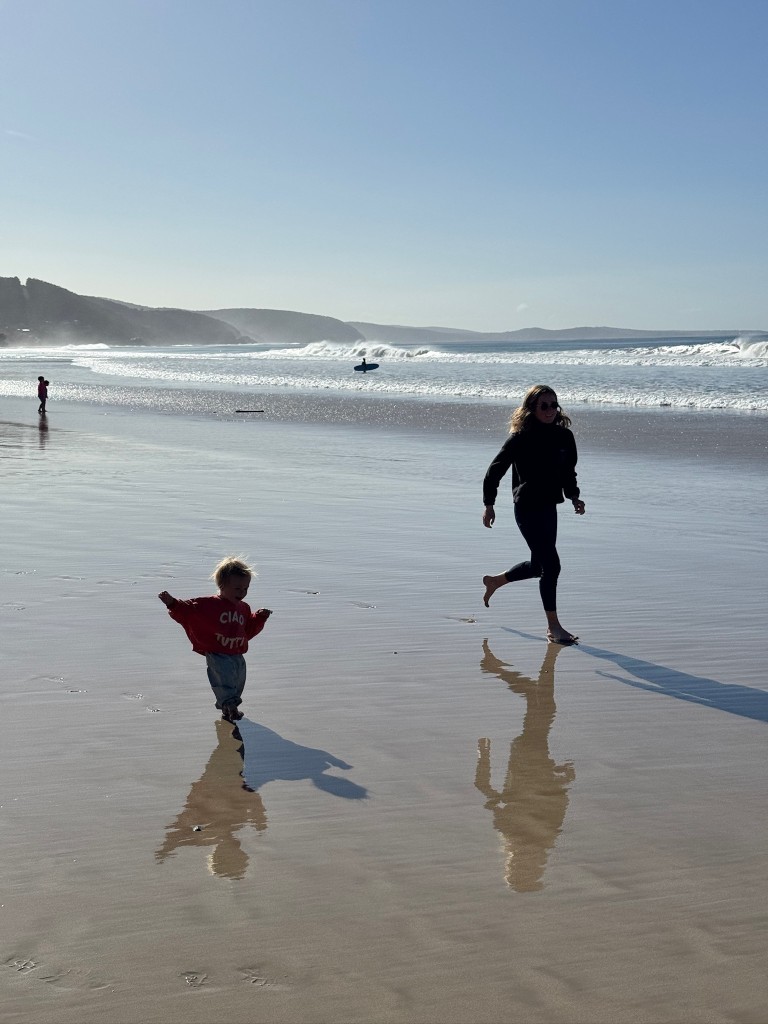 Toddler and adult running on wet sand along the shoreline